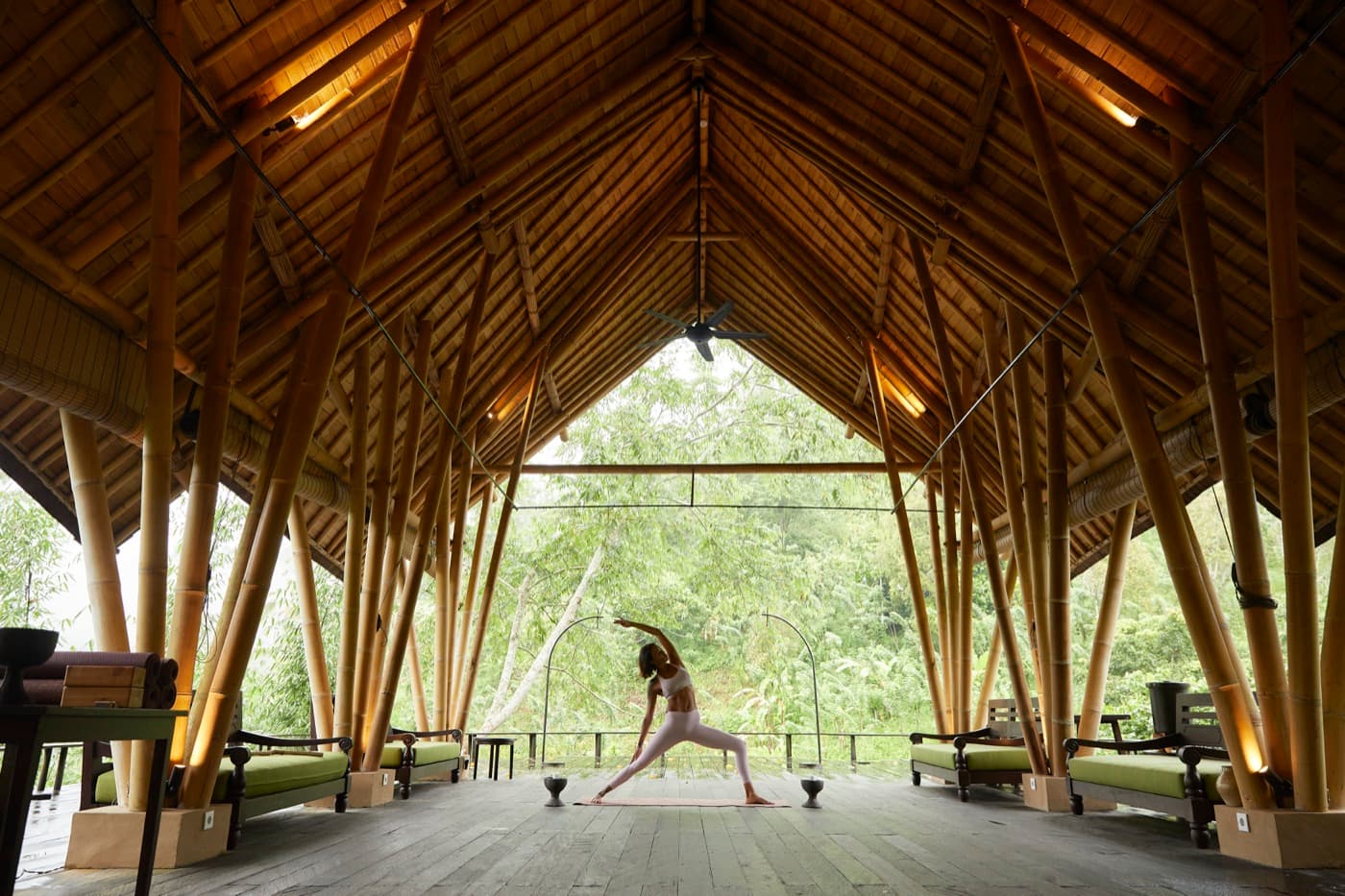 Kimberley practising a wide reverse warrior pose inside an open bamboo pavilion, jungle filling the view beyond.