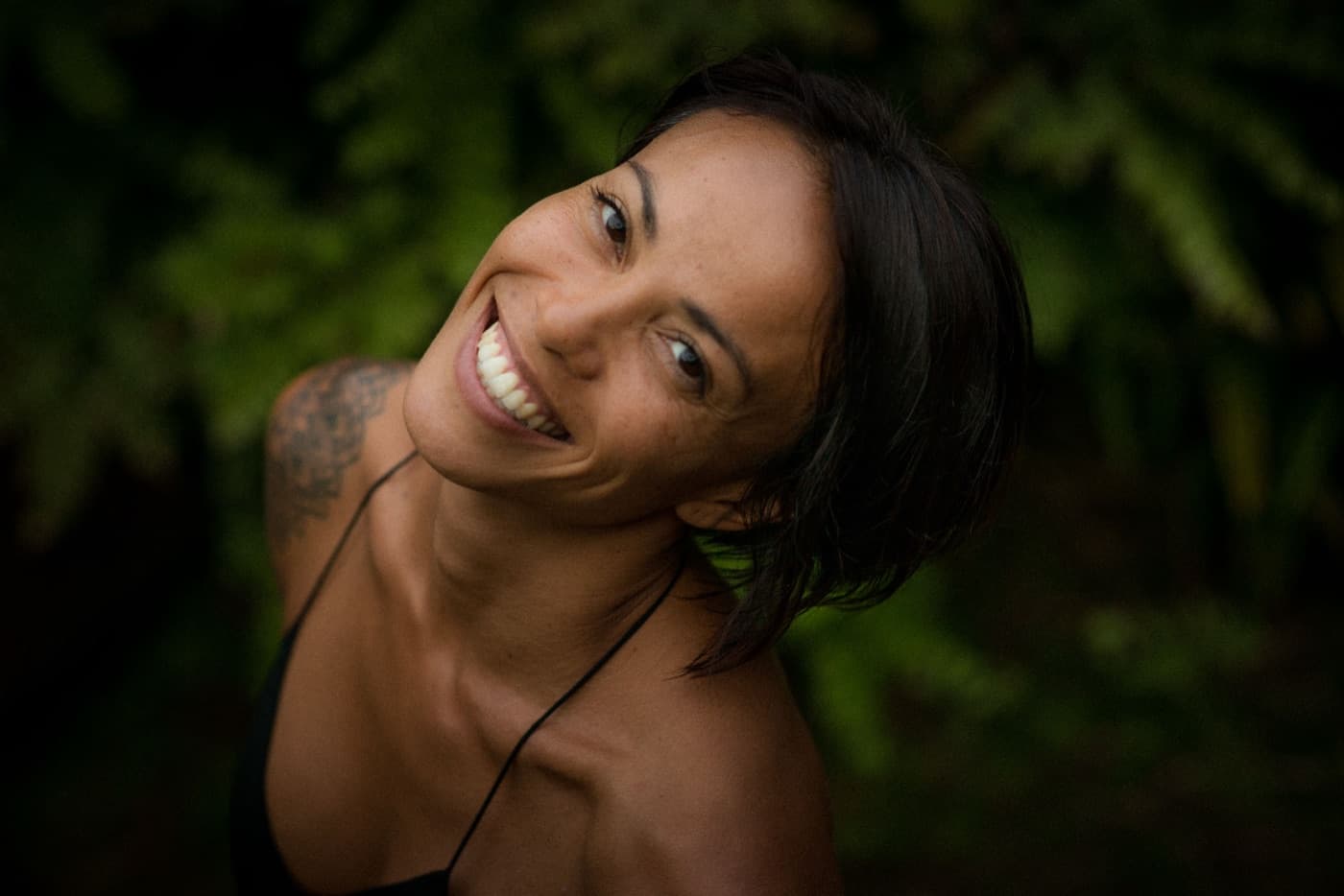 Kimberley Utama laughing warmly with her head tilted back, jungle greenery behind her.