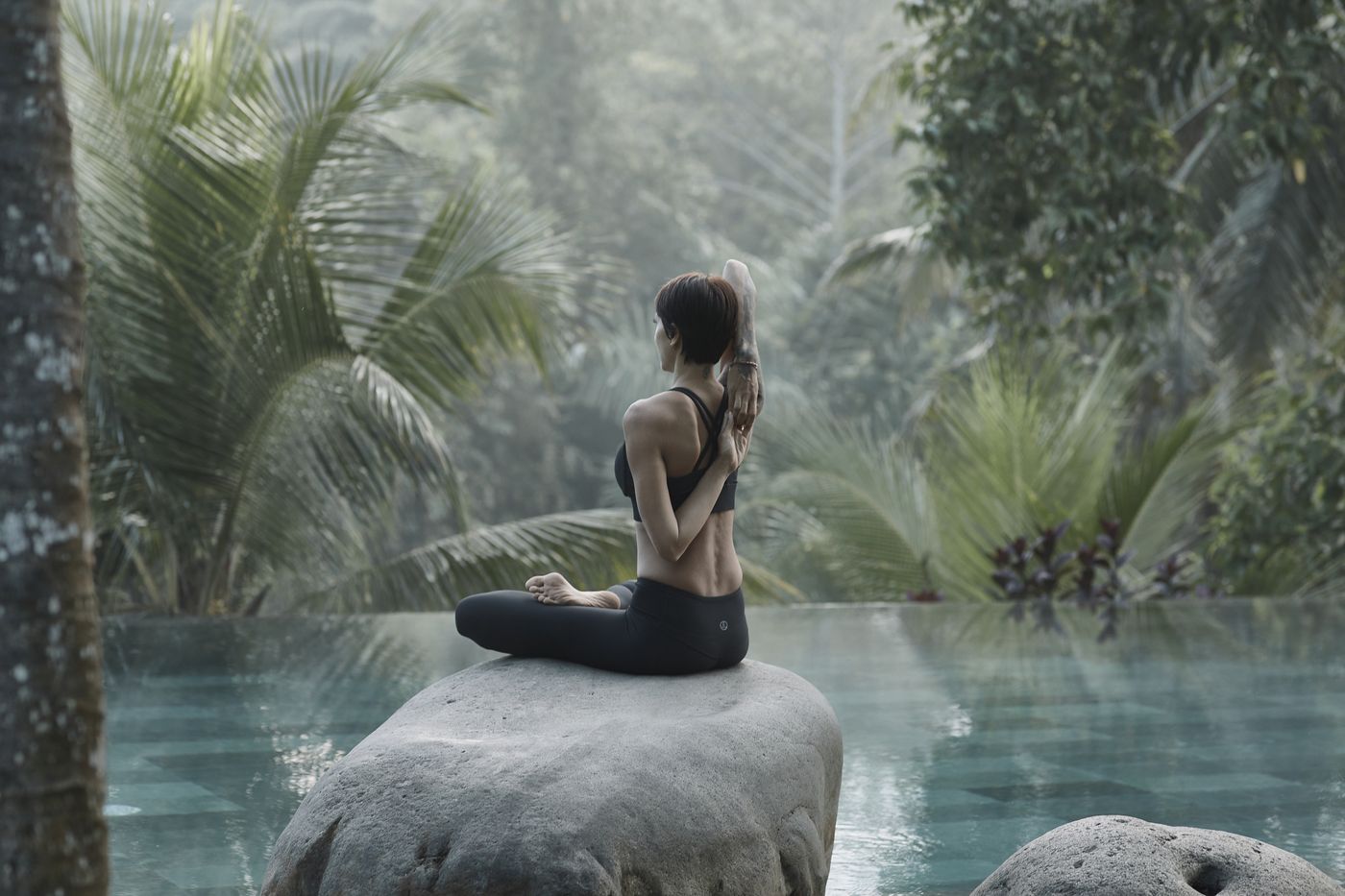 Kimberley sitting cross legged on a rock overlooking a still pond, jungle surrounding her