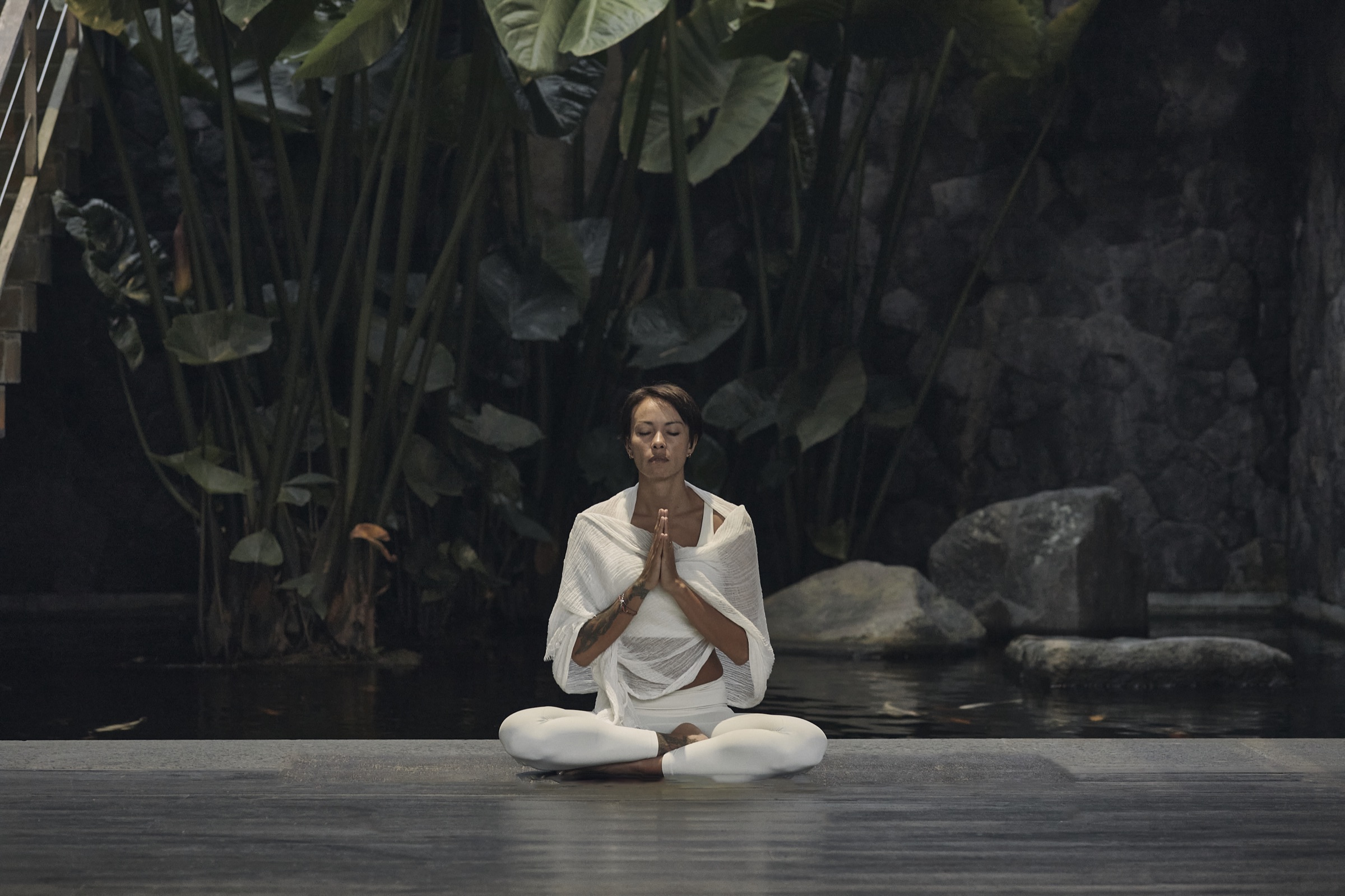 Kimberley Utama seated in meditation beside a still pond in Ubud, Bali.